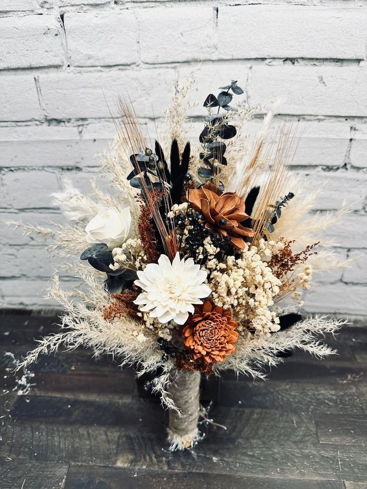 a vase filled with flowers and feathers on top of a wooden floor next to a brick wall