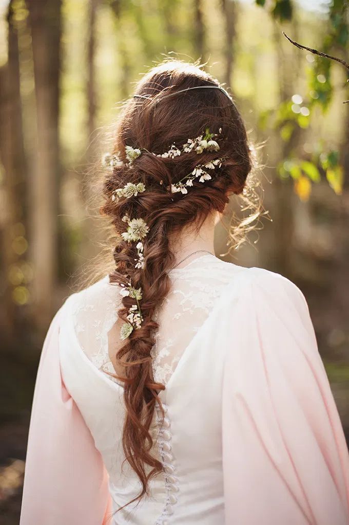 a woman with long hair wearing a pink dress and flower in her hair is standing in the woods