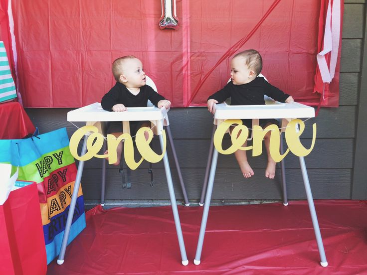 two toddlers sitting in high chairs with one sign on the table that says one