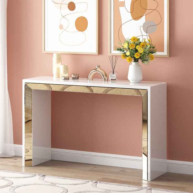 a white console table with flowers on it in front of two pictures hanging on the wall