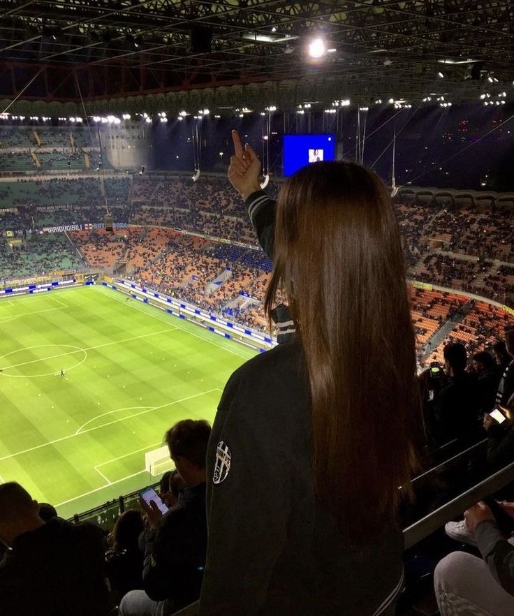 a woman standing in front of a crowd at a soccer stadium with her hand up to the sky