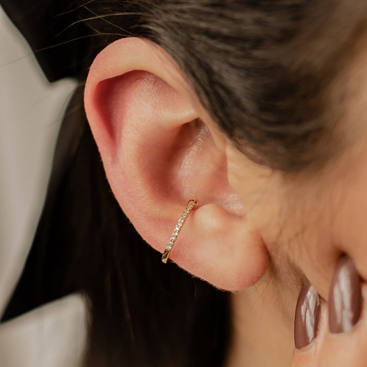 This ear cuff is made from 18 karat gold-plated sterling silver and consists of a single band with squared edges, half covered with tiny white zircon stones embellishing the outer surface. It has a small gap in the band where it fits onto the ear, and two metallic balls on either side of the gap to hold it securely in place. Simple yet sophisticated, this is a versatile piece that will add the perfect amount of extra sparkle to an outfit.  DETAILS: Diameter: Outer diameter: 1.4 cm Weight: 1.0 g Material: 18 k gold plated, 925 Sterling Silver 🏷️ This product is made of sterling silver -- easily recognizable by its '925' stamp of authenticity. It is also hypoallergenic, making it suitable for people with sensitive or irritable skin. We recommend avoiding perfume, deodorant or other chemical 14k White Gold Single Ear Cuff, Fine Jewelry Yellow Gold Single Ear Cuff, Elegant 14k Gold Single Ear Cuff, Gold Plated Single Ear Cuff Fine Jewelry, Gold Plated Ear Cuff Fine Jewelry, Elegant Hypoallergenic Huggie Ear Climbers, Rose Gold 14k Gold Ear Cuff, Gold Plated Fine Jewelry Cartilage Earrings, 14k Gold Pierced Ear Cuff Fine Jewelry