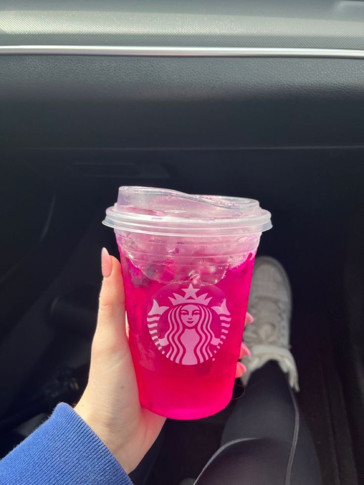 a person holding up a pink starbucks cup in their hand while sitting in a car