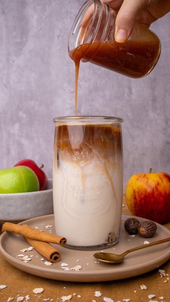 someone is pouring caramel into a glass full of milk on a plate with apples in the background