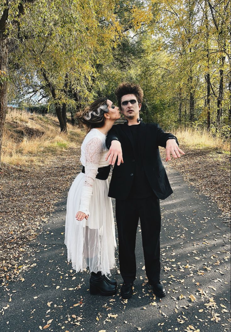 a man and woman dressed up in costumes standing on a road with trees behind them