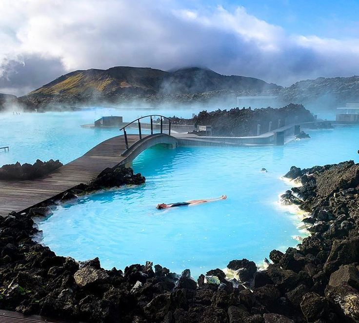 a man swimming in a blue lagoon surrounded by rocks and water with mountains in the background