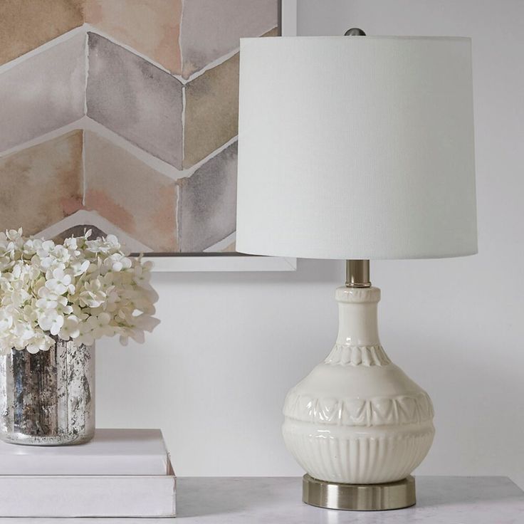 a white lamp sitting on top of a table next to a vase filled with flowers