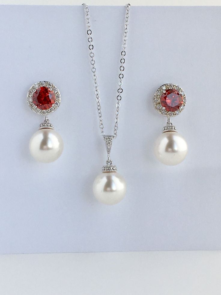 I've created this elegant red ruby cubic zirconia and pearl bridal jewelry set in rhodium plated brass setting and the set includes: # Earrings feature large 12mm Swarovski pearls that dangle from brilliant cut red ruby cubic zirconia with halo setting 12mm ear stud. Halo setting gives a brilliantly beautiful effect. Total length of the earrings is 2.8 cms. #Classic pearl bridal necklace and pendant set with rhodium plated brass peg and bail. Necklace features a pendant with large 12mm Swarovski Formal Pearl Drop Jewelry Sets With Cubic Zirconia, Anniversary Jewelry Sets With Pearl Drop And Cubic Zirconia, Elegant Ruby Bridal Set For Wedding, Red Elegant Jewelry With Pearl Pendant, Elegant Red Jewelry With Pearl Pendant, Red Cubic Zirconia Jewelry Sets, Fine Jewelry Lab-created Ruby Necklaces For Wedding, Lab-created Ruby Necklaces For Wedding, Fine Jewelry Lab-created Ruby Necklace For Wedding