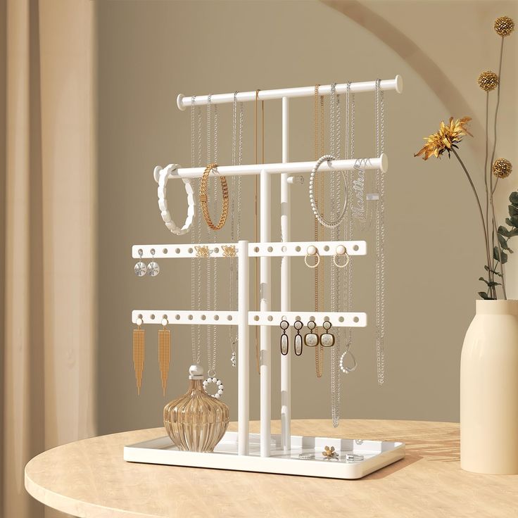 there is a white jewelry rack with earrings on it and a vase with flowers in the background