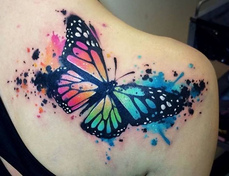 a colorful butterfly tattoo on the back of a woman's shoulder