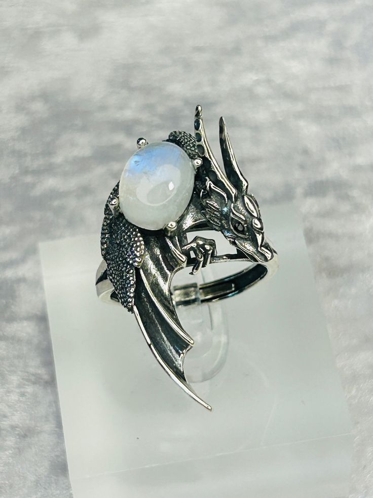 This ring is absolutely beautiful. High Detailed Dragon Ring With Prong Set Smooth Rainbow Moonstone Gemstone - Supplied With Gift Box. Ring is lovingly made of 925 Silver & Stamped 925 The beautiful Moonstone Cabochon Measures 13.6mm x 10.5mm and has a Beautiful Blue Flashes. The ring can adjusted from the back, but please be gentle when you adjust, so as not to damage the shape of the ring. The Dragon Design itself Measures 40mm tall x 24.8mm wide. Black Spinel Crystals have been used for the Mystical Gemstone Rings For Formal Occasions, Hallmarked Moonstone Jewelry For Wedding, Hallmarked Moonstone Wedding Jewelry, Silver Mystical Moonstone Ring, Mystical Adjustable Oval Jewelry, Mystical Moonstone Open Ring Jewelry, Mystical Gemstone Rings For Collectors, Mystical Collectible Gemstone Rings, Adjustable Mystical Sterling Silver Rings