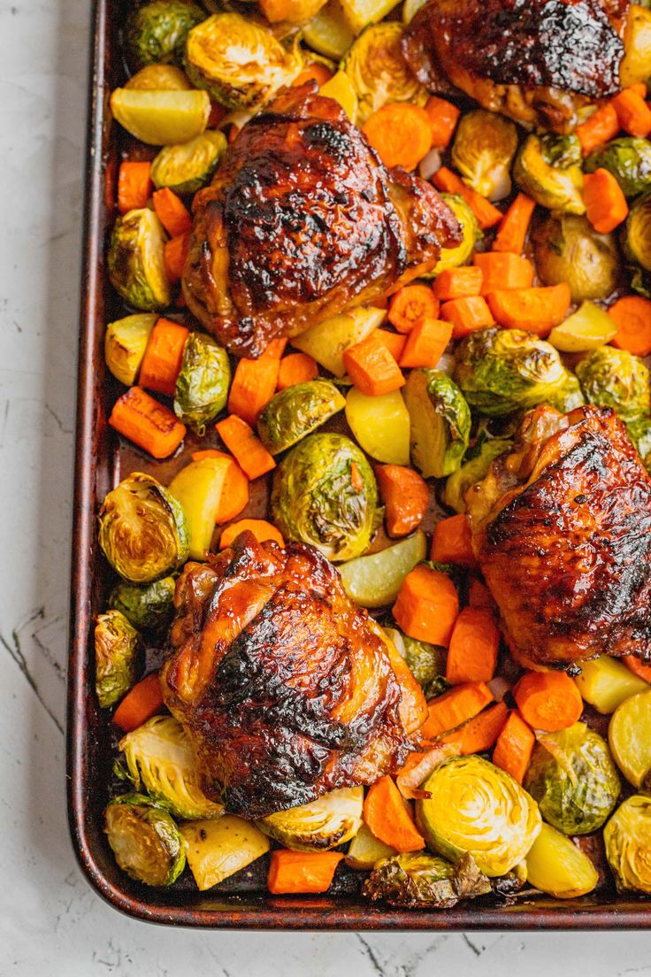 chicken, brussels sprouts and carrots in a roasting pan on a marble surface