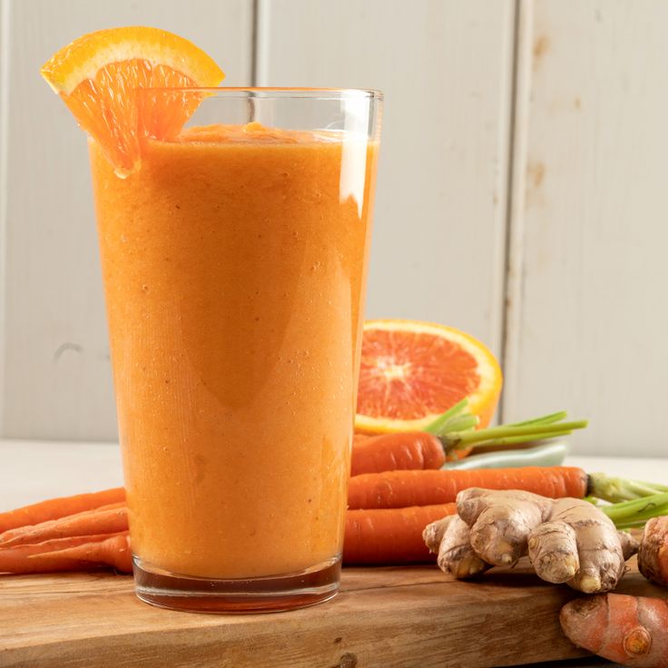 an orange smoothie in a glass next to carrots and ginger