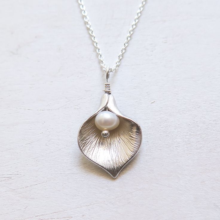 Silver Calla Lily Necklace - Gift for Her Classic and elegant gift for mother, friend or for bridesmaids. Dainty, easy to wear everyday or on special occasions. FEATURES: * A small freshwater pearl is wire wrapped with bright calla lily petal to form a flower pendant. * The petal is rhodium plated over brass. * Comes with sterling silver chain, finished with spring clasp closure. All sterling silver calla lily necklace: https://www.etsy.com/listing/476943360/ MEASUREMENTS: * the pendant is about Elegant Birth Flower Jewelry For Anniversary, Classic Wedding Jewelry With Birth Flower, Silver Birth Flower Necklace For Wedding, Elegant Birth Flower Jewelry, Elegant Flower Shaped Necklace For Mom, Elegant Birth Flower Jewelry For Wedding, Elegant Wedding Jewelry With Birth Flower Detail, Elegant Wedding Jewelry With Birth Flower, Elegant Birth Flower Jewelry For Mother's Day