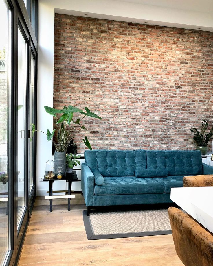 a living room filled with furniture and a brick wall behind the blue couch is a potted plant