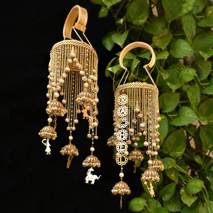 two golden bells hanging from a tree with green leaves in the background and one has a dog on it