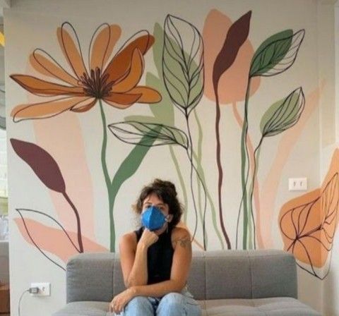 a woman sitting on top of a couch next to a wall with flowers painted on it