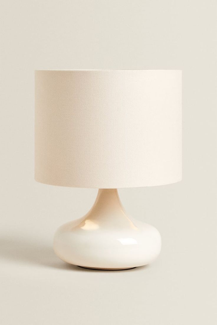 a white table lamp with a cream shade on it's base, against a plain background