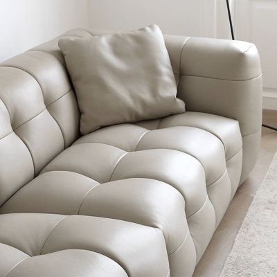 a white leather couch sitting on top of a wooden floor next to a lamp and rug