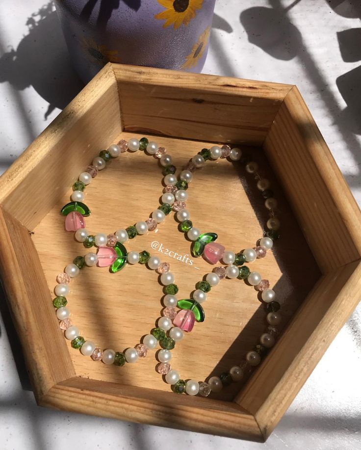 a wooden box with beads and flowers in it on a table next to a potted plant