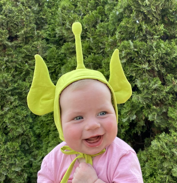 a smiling baby wearing a yellow hat with horns on it's head and ears