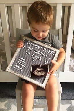 a young boy sitting in a chair holding a sign that says i'm going to be a big brother to twins