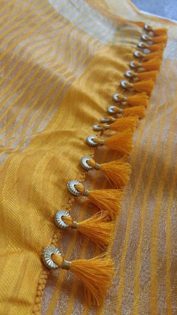 an orange and yellow striped fabric with tassels on the edges, along with silver beads