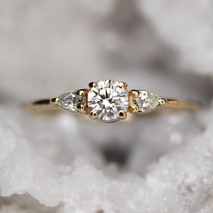 a three stone diamond ring sitting on top of a white rock with snow flakes around it