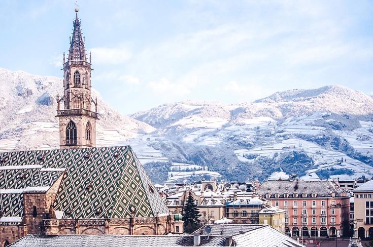 a large building with a steeple in the middle of it and snow covered mountains behind it