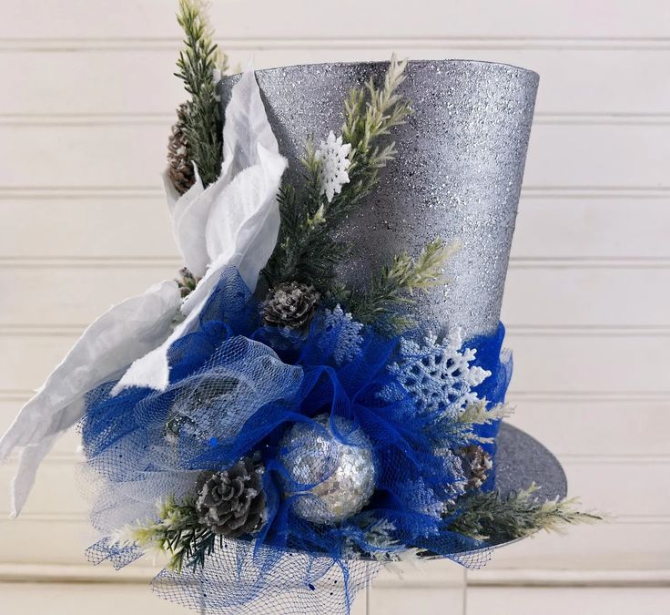 a silver top hat decorated with blue and white flowers, pine cones and snowflakes