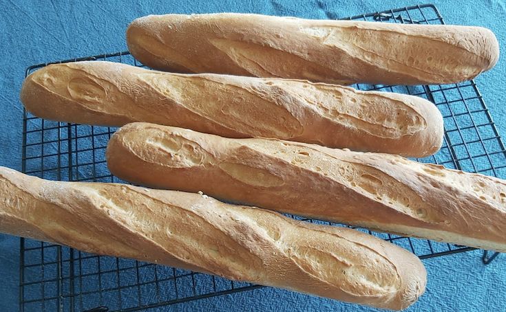 four loaves of bread sitting on top of a cooling rack in front of a blue towel