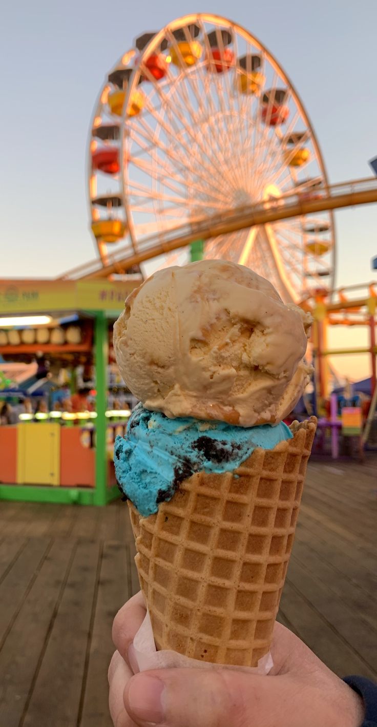 a person holding an ice cream cone in front of a ferris wheel