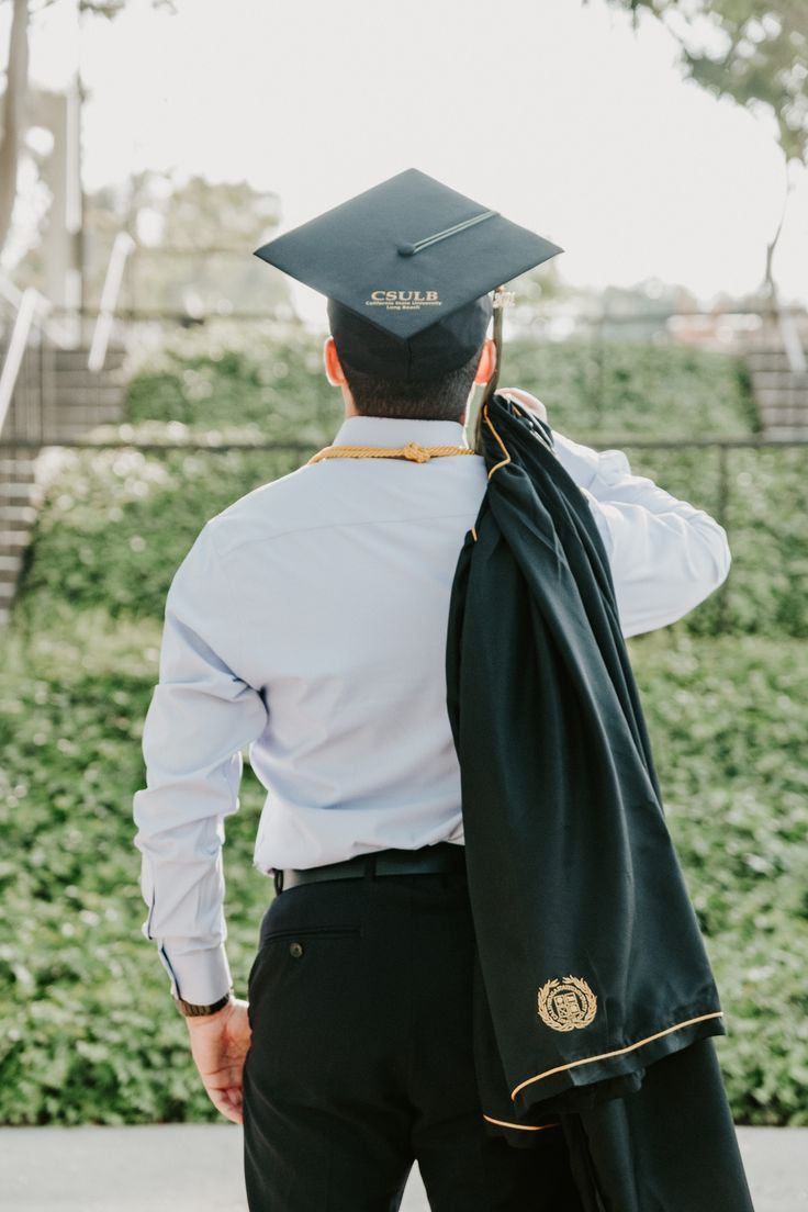 a man in a graduation cap and gown is holding his coat over his shoulder as he walks down the street