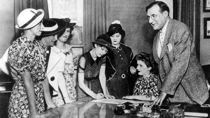 a group of people sitting around a table in front of a man with long hair