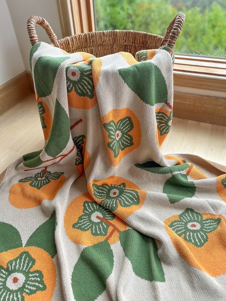 an orange and green flowered blanket sitting on top of a wooden floor next to a basket