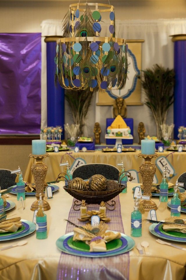 the table is set with blue and gold plates, place settings, and peacock decorations