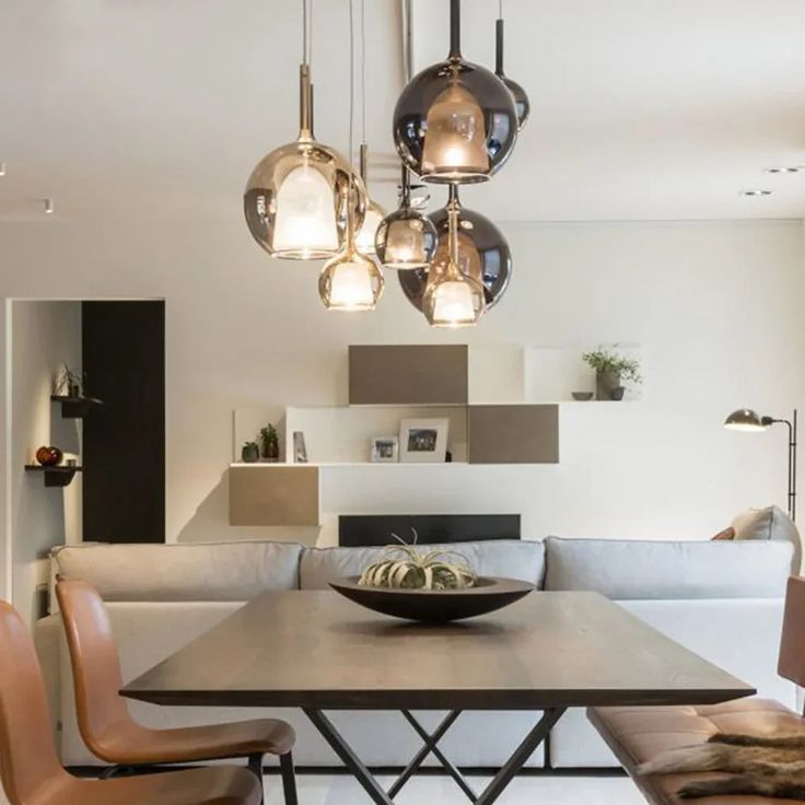 a dining room table with chairs and lights hanging from it's ceiling in front of a couch