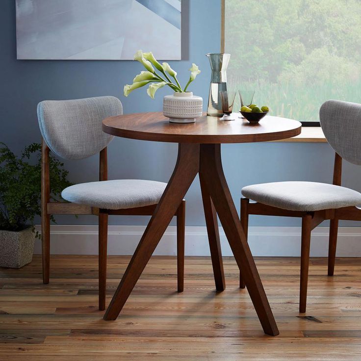 two chairs sitting at a table in front of a window with a vase on it