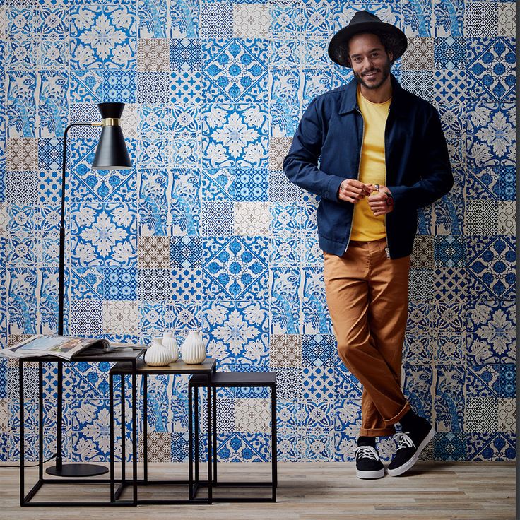 a man standing in front of a blue and white wall with a lamp next to it