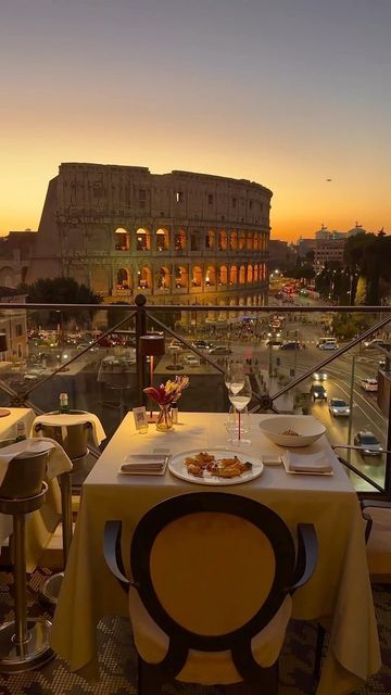 an outdoor dining area overlooking the roman colossion at sunset, with tables and chairs set for two