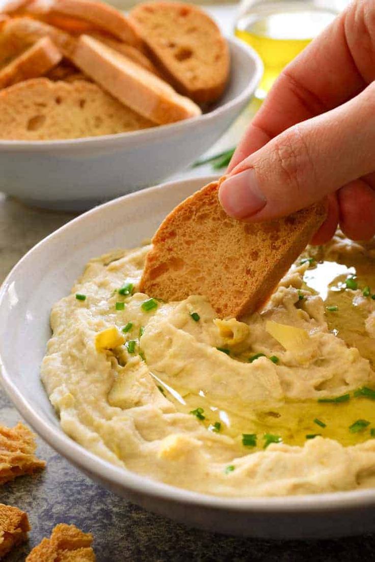 a person dipping some bread into a bowl of hummus and crackers on the side