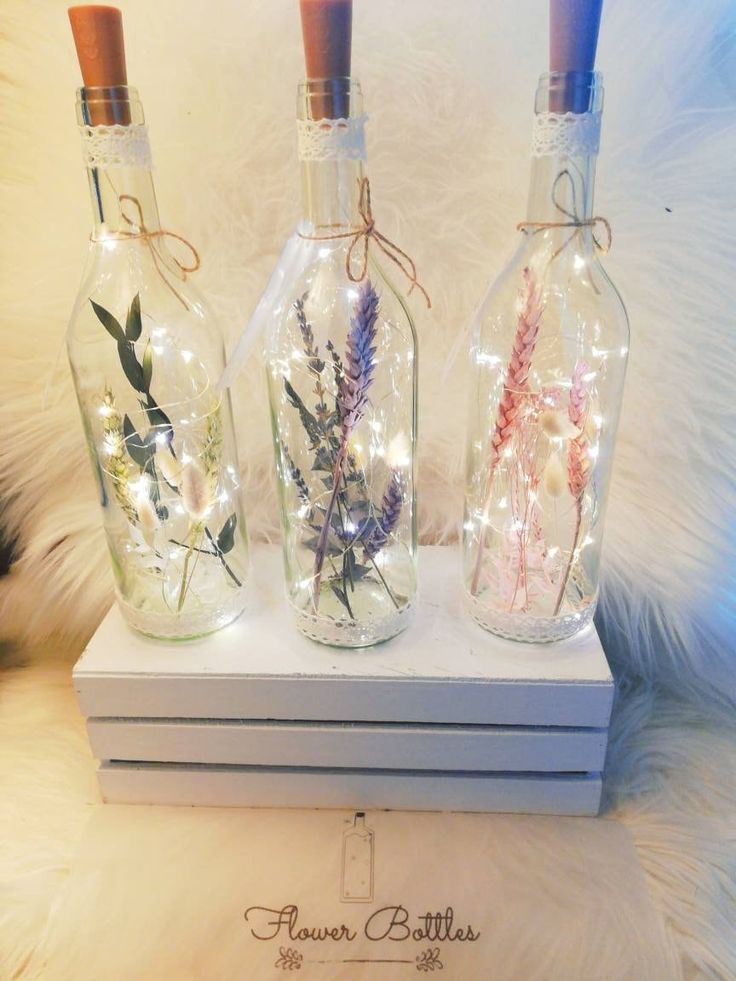 three glass bottles with flowers in them are sitting on top of a white box that is lit up