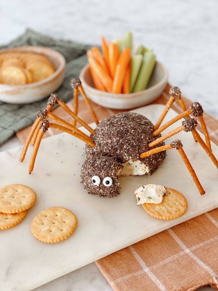 a spider made out of crackers and carrots on a white plate next to other snacks