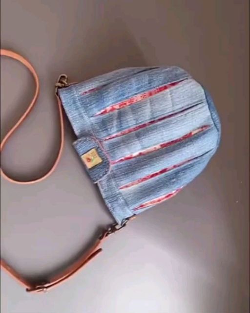 a denim purse with an orange strap hanging from it's side on a table