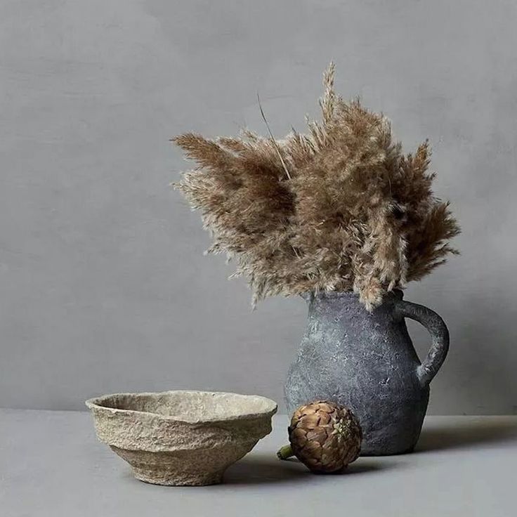 a vase and bowl are sitting next to each other on a gray surface, one is made out of clay