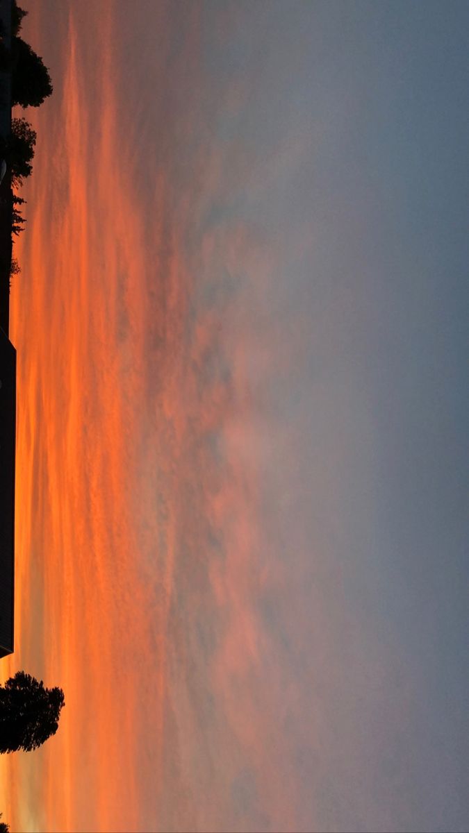 the sun is setting behind some clouds in the sky over a building and tree line