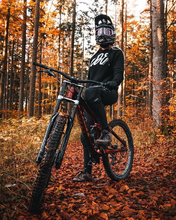 a person sitting on top of a bike in the woods with leaves all around them