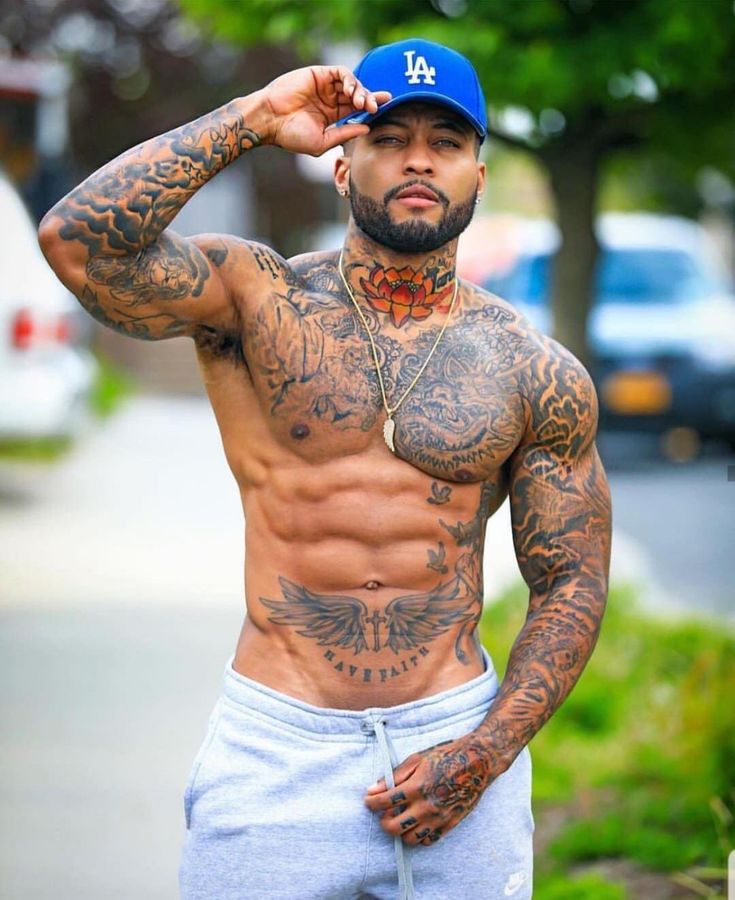 a shirtless man with tattoos on his chest and hands behind his head is posing for the camera