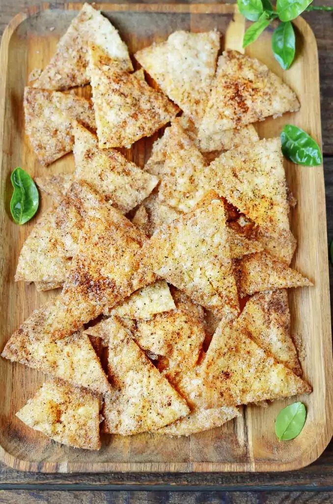 homemade tortilla chips on a wooden cutting board with basil sprigs in the background