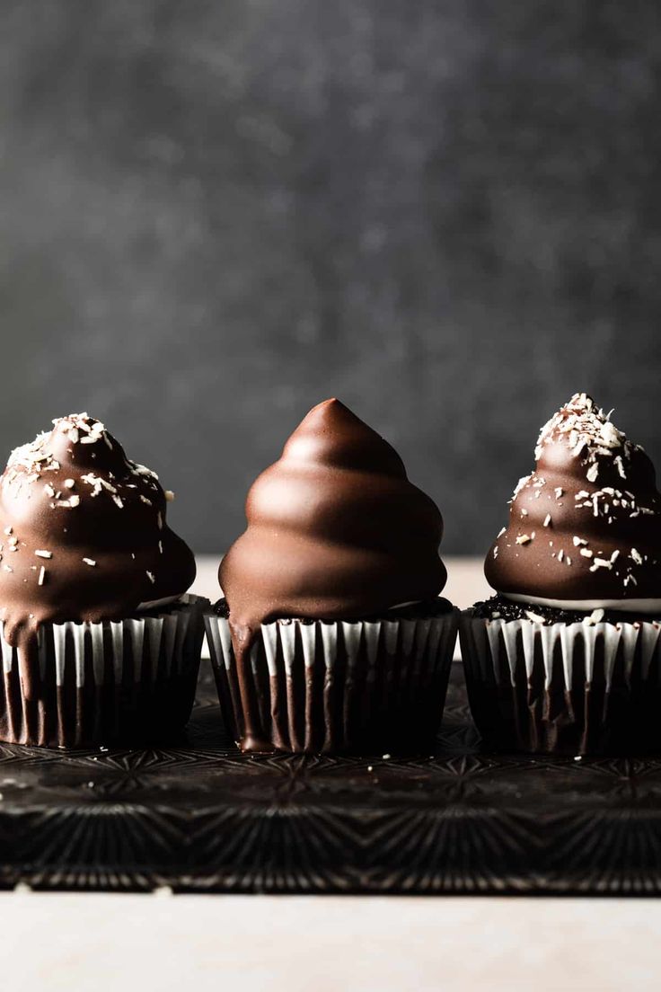 three chocolate cupcakes with sprinkles on top sitting on a black plate